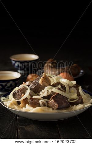 National Kazakh dish - Beshbarmak prepared with meat and pasta on the dark wooden table