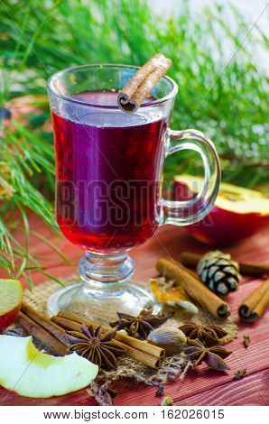 Spicy Christmas drink in a glass with spices on a background of trees