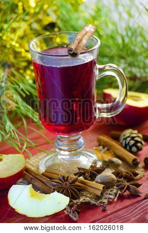 Spicy Christmas drink in a glass with spices on a background of trees