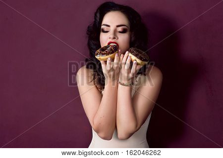 young, beautiful, attractive, darkhaired woman with colorful, tasty, glazed doughnuts on marsala background