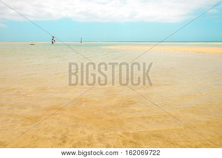 View on the beach Sotavento the lagoon with clear sea water and windsurfers cloudy sky and golden sand. Location Playa de Sotavento Canary Island Fuerteventura Spain.