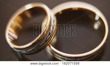 Golden wedding rings on mirror glasses table - one lies on top of another, macrom, horizontal, close up