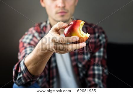 Man holds apple. Young male person with red bitten apple in hand