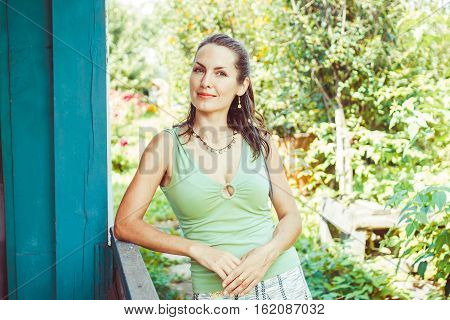 a girl stands on the porch of the house among the branches of trees in summer