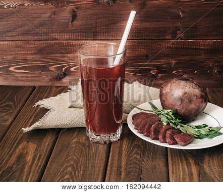 glass of fresh beet juice, dish with beets and greens on a dark rustic wooden background