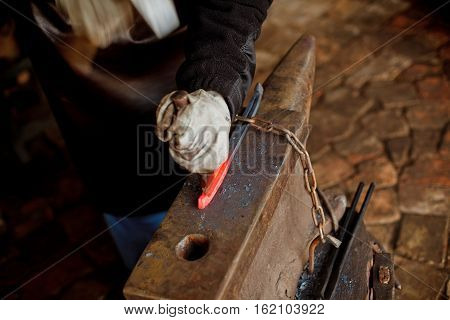 The blacksmith manually forging the molten metal on the anvil in smithy with spark fireworks