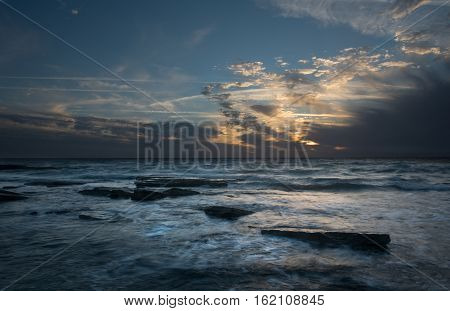 Rocky beach with seawaves crashing at the rocks during sunset