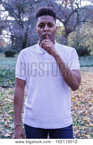 Young black African man sending silence. He puts his finger to his lips as a gesture to silence.