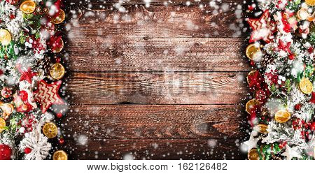 Merry Christmas Frame with Snow and wood green pine, colorful baubles, knots with berries,stars, orangesand other seasonal stuff over an old wooden aged background