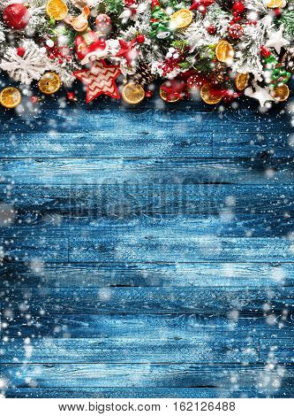 Merry Christmas Frame with Snow and wood green pine, colorful baubles, knots with berries,stars, orangesand other seasonal stuff over an old wooden aged background