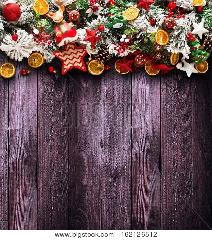 Merry Christmas Frame with green pine, colorful baubles, knots with berries,stars, orangesand other seasonal stuff over an old wooden aged background