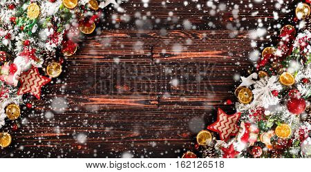 Merry Christmas Frame with Snow and wood green pine, colorful baubles, knots with berries,stars, orangesand other seasonal stuff over an old wooden aged background