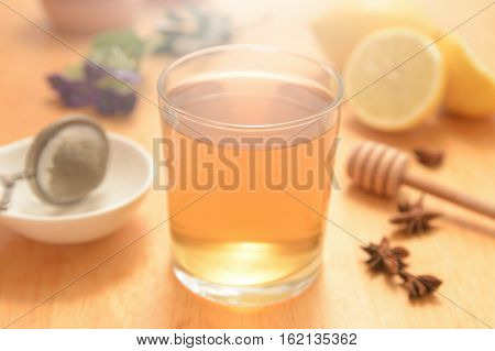 A glass of camomile with some natural honey and anise seeds on a wooden table of a rustic kitchen. Some citrics and herbalist remedies.