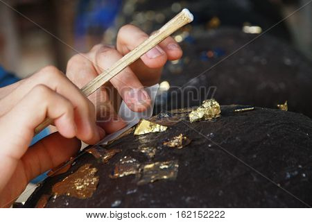 Buddhists make meritGilding gold leaf to round stones embedded call LukNimitr for worship Buddha. Selective focus.