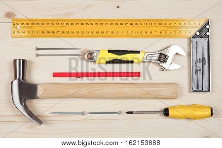 Set of working tools: Right angle square tool, knife, hammer, yellow adjustable wrench, red pencil, screwdriver and nails on the wooden background
