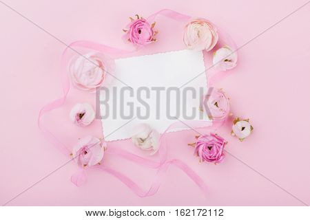 White paper blank and spring flower on pink desk from above for wedding mockup or greeting card on womans day. Floral frame in flat lay style.