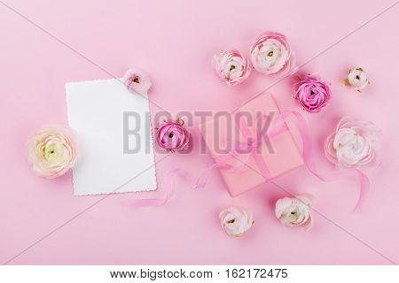 Gift or present box white paper blank and beautiful spring flower on pink desk from above for wedding mockup or greeting card on womans day in flat lay style.