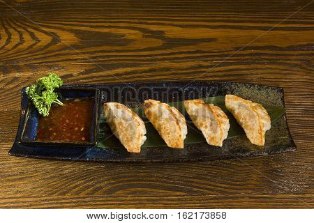 Yaki gedza with sauce in a ceramic pot on a wooden table