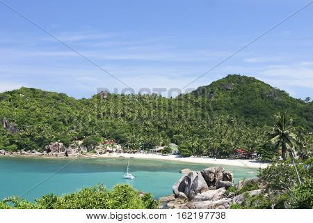 white sailboat anchored in beautiful crystal bay surrounded by jugle clad hills near lamai on ko samui island in the gulf of thailand