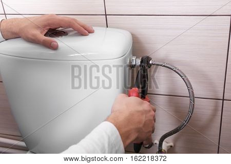 Plumber fixing water hose on toilet cistern, closeup