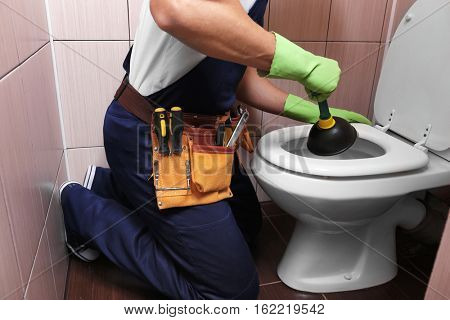 Plumber repairing toilet with hand plunger, closeup