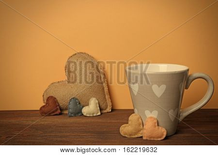 Cup with color hearts on wooden table against beige background