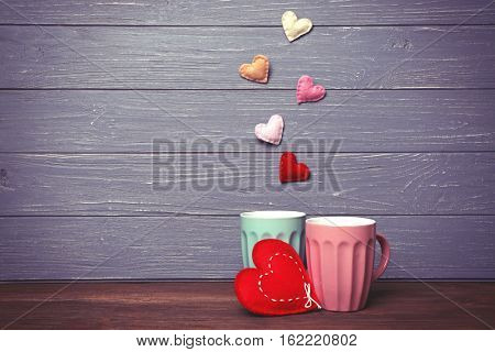 Two cups and color hearts on wooden background