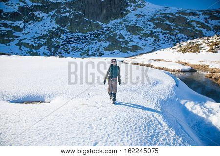 brunette sport active woman with green vest red sweater brown trousers walking hiking in snow with blue sky in Gredos mountain Avila Spain Europe