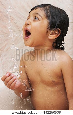 Happy baby in the bath drinking water from shower Water splash