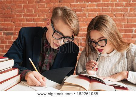 Portrait of man and woman studying at library. Pair of young students in glasses doing pair graduation project at library. Teamwork, education, brainstorm concept