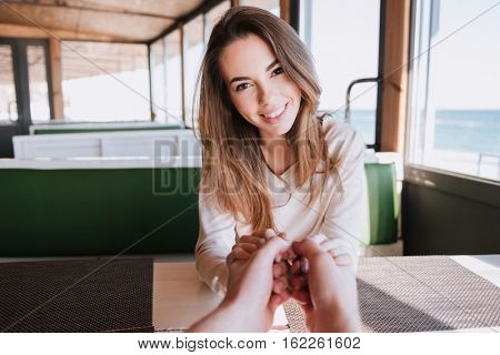 Smiling woman on date holding hands her man in cafe near the sea. First-person view