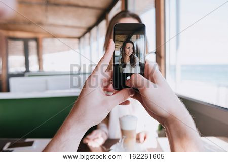 First-person view of man making photo his woman on date in cafe near the sea