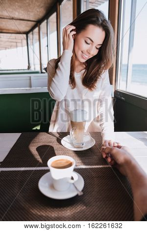 Vertical image of woman on date with man sitting by the table with coffee in cafe near the sea. First-person view
