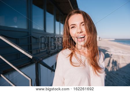 Happy Woman in sweater standing on beach near the sea
