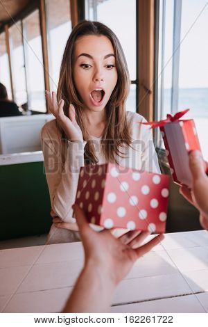 Vertical image of surprised woman sitting by the table in cafe and gets the gift. First-person view