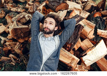 Man having rest on pile of wood top view. Young guy dreaming on bunch with firewood. Hard work, relax, handyman, country lifestyle concept