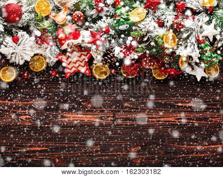 Merry Christmas Frame with Snow and wood green pine, colorful baubles, knots with berries,stars, orangesand other seasonal stuff over an old wooden aged background