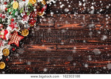 Merry Christmas Frame with Snow and wood green pine, colorful baubles, knots with berries,stars, orangesand other seasonal stuff over an old wooden aged background