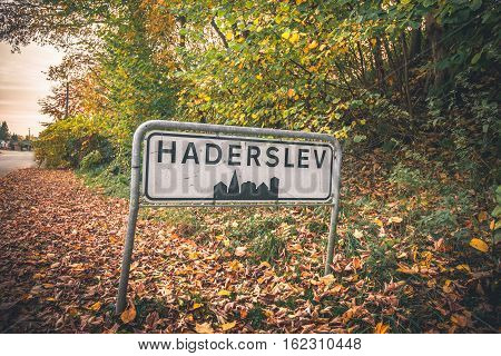Haderslev city sign by a road in Denmark in the fall with colorful trees and leaves on the groubd