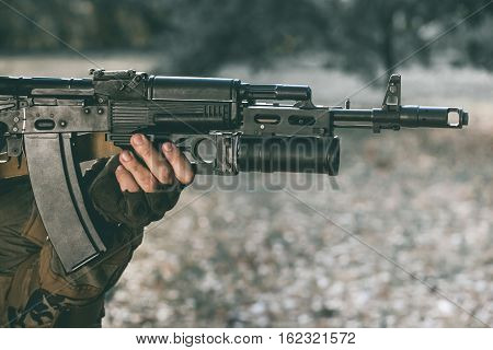 The soldier in the performance of tasks in camouflage and protective gloves holding a gun. War Zone.