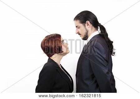 Stand off between a male and female partner with the shorter woman staring up belligerently into the face of the man in a suit with a ponytail profile view on white