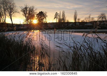The bright rays of the setting sun glide over the ice of a small lake.