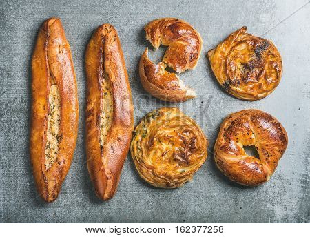 Oriental style Turkish pastry with different fillings over grey stone background, top view. Bagels with black sesame, borek with spinach and poppy seeds, pizza pide with cheese