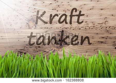 German Text Kraft Tanken Means Relax. Spring Season Greeting Card. Bright, Sunny And Aged Wooden Background With Gras.