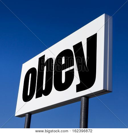 Horizontal billboard with the order to OBEY against irreal blue sky. Abstract concept of consumerism human mind control power of corporations and lobbies.