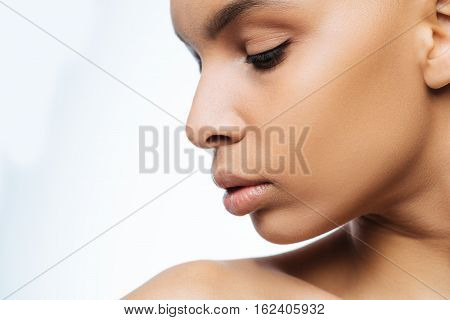 Full of grace. Elegant graceful pleasant Negroid woman looking down while standing isolated in white background and expressing grace