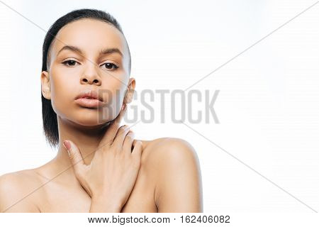 My soft skin. Charming graceful young Negroid woman touching her skin while standing against white background and expressing femininity