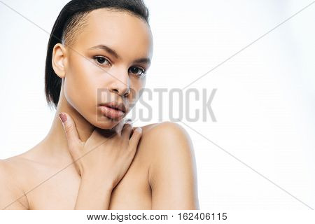 Full of concentration. Pleasant graceful young Negroid woman touching her neck while standing isolated in white background and expressing elegance