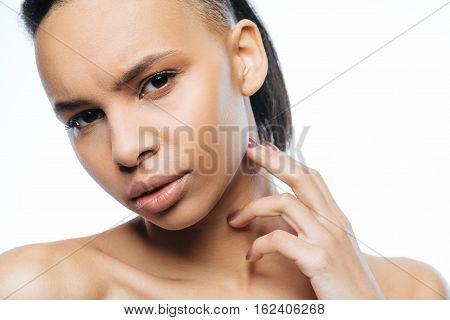 Full of interest. Elegant concentrated young Negroid woman touching her neck while standing against white background and expressing interest