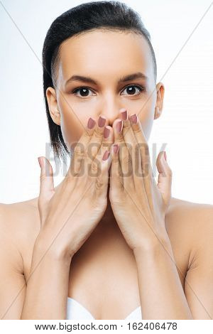 Full of surprise. Surprised amazed young Negroid woman closing her mouth with hands while standing against white background and expressing amazement
